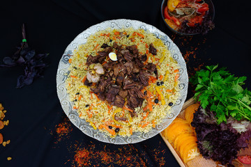 Pilaf and ingredients on plate with oriental ornament on a black background. Central-Asian cuisine - Plov Top view