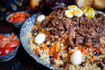Pilaf and ingredients on plate with oriental ornament on a black background. Central-Asian cuisine - Plov Top view