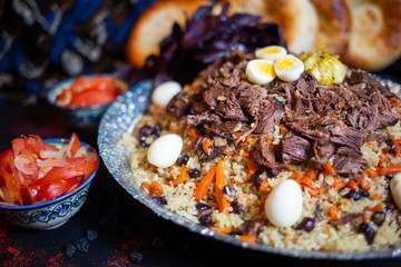 Pilaf and ingredients on plate with oriental ornament on a black background. Central-Asian cuisine - Plov Top view