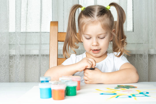 what to do for a child during the period of quarantine and self-isolation, 4 years old girl opens a jar of gouache and smiles. in front of it are many cans of colored paints and a drawing