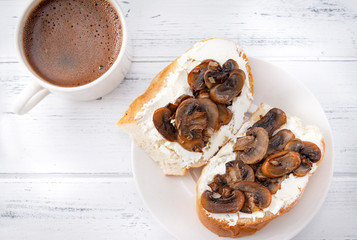 sandwiches with soft cheese and mushrooms on a plate, a Cup of black coffee on a white wooden background, Breakfast