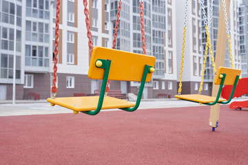 Swing for children on a new playground against the background of a new apartment building