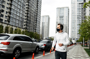 Fototapeta na wymiar Keep yourself in shape during quarantine. Athletic young man is jogging in a protective mask among high-rise buildings. Healthy lifestyle concept