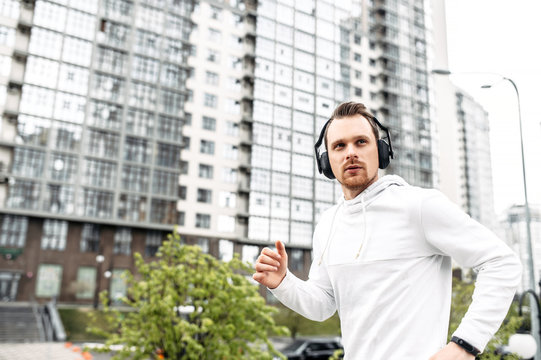 Workout outdoors. Young athletic guy in sportswear with headphones runs in an urban landscape