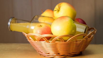 A large bottle of apple juice and fresh apples in a basket on the table.