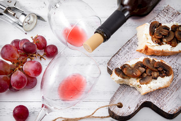 2 glasses,  bottle of red wine, corkscrew, grapes, snacks with cheese and mushrooms on a white wooden