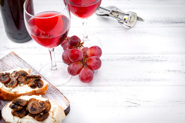 glasses of red wine, ,  bottle  , grapes, corkscrew,  snacks with mushrooms  and  cheese   on a...