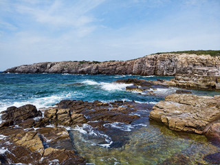 High cliffs and rocks hit by sea waves, white foam from the ocean and emerald waters in this wilderness area shows its power