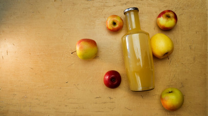 Background with a big bottle of apple juice and fresh apples that lie on the table.