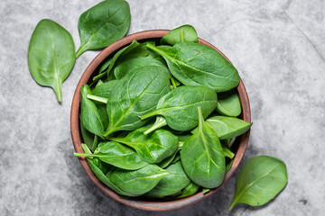 Fresh organic baby spinach leaves in a clay bowl on dark stone table close up. Tasty diet food concept.