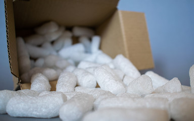 Open cardboard box with white styrofoam filling pieces comming out, parcel packing materials, safe and secure shipment methods, grey background