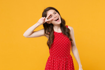 Cheerful young brunette woman girl in red summer dress posing isolated on yellow wall background studio portrait. People sincere emotions lifestyle concept. Mock up copy space. Showing victory sign.