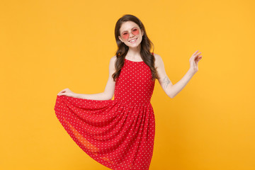 Smiling young brunette woman girl in red summer dress, eyeglasses posing isolated on yellow wall background studio portrait. People emotions lifestyle concept. Mock up copy space. Looking camera.