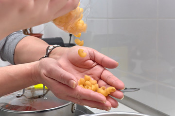 Mujer vertiendo la pasta de los macarrones en la cazuela con agua, aceite y laurel.