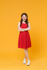 Cheerful young brunette woman girl in red summer dress posing isolated on yellow wall background studio portrait. People sincere emotions lifestyle concept. Mock up copy space. Holding hands crossed.