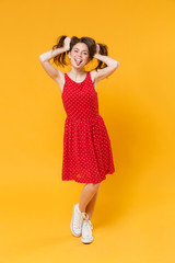 Funny young brunette woman girl in red summer dress posing isolated on yellow wall background studio portrait. People lifestyle concept. Mock up copy space. Holding hair like ponytails showing tongue.