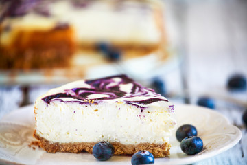 A slice of delicious homemade blueberry marble cheesecake with graham cracker crust and fresh blueberries. Selective focus with extreme shallow depth of field.