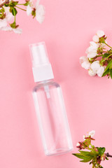 bottle with transparent liquid. alcohol hand sanitizer over pink background with flower decoration.