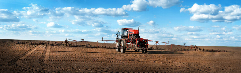 Panoramic view of self-propelled red sprayer in the field makes fertilizers in early spring