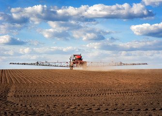 Big red sprayer with long arms at the arable field makes fertilizers in early spring view with...
