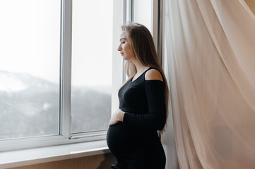 A pregnant girl is breathing fresh air from the window