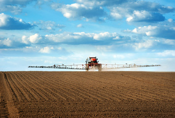 Big red sprayer with long arms at the arable field makes fertilizers in early spring view with...