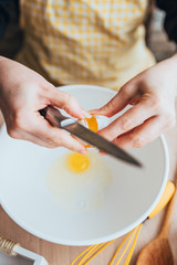 A woman is preparing a custard dough for baking - breaks an egg in a bowl - home cooking