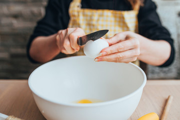Fototapeta na wymiar A woman prepares a dough for baking - breaks an egg in a bowl - home cooking