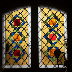 Mosaic colored stained glass window with an ornament located in an old building. there is a vase of dried flowers on the windowsill. there are light highlights on the glass