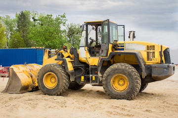 Fototapeta na wymiar Yellow heel loader excavator on sand against construction. Heavy equipment on background sky
