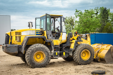 Obraz na płótnie Canvas Yellow heel loader excavator on sand against construction. Heavy equipment on background sky