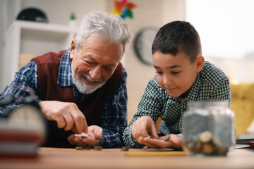 Grandpa and grandson saving money. Grandfather teaching grandchild how to save money.	