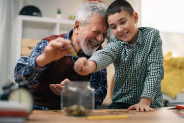 Grandpa and grandson saving money. Grandfather teaching grandchild how to save money.	