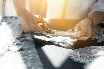 Hands girls seamstresses who cut the Golden scissors lace fabric at the table. Outside the window...