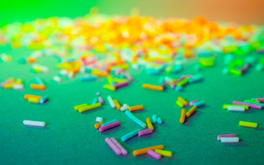 Cake decorating sweets, green and orange background, baking colorful sprinkles, home baking decorations, copy spce for text, bright colors, pile of sugar decorations, multicolored sweet pieces