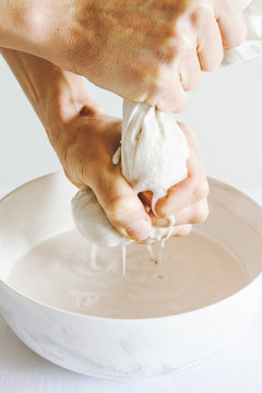 Preparation Of A Plant-based Nut Milk With Hands Straining The Milk Through A Milk Bag. White Background