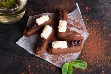 Chocolate rum balls with green mint tea on dark background. Brown sweets with cream