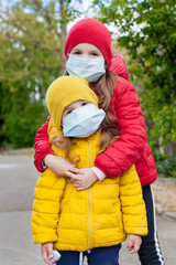 Portrait of children girls walking near the house in a disposable protective face mask