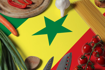 Senegal flag on fresh vegetables and knife concept wooden table. Cooking concept with preparing...