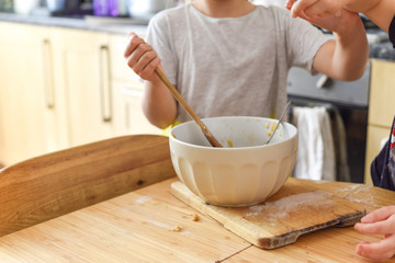 Children cooking stirring a mixing bowl in the kitchen at home while baking cookies