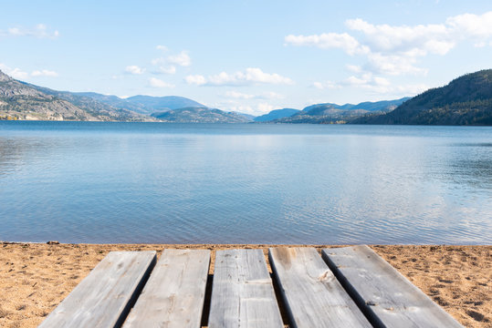 Picnic table on sandy beach with view of lake, mountains, and blue sky © Amy Mitchell