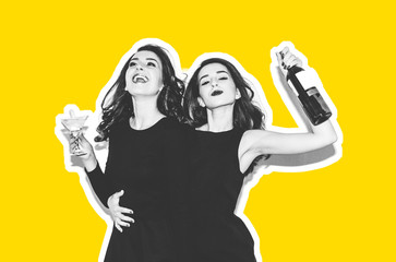 Two brunette sisters with long hair are drinking alcoholic cocktail and wine. Two beautiful girls in evening dress laughing and smiling. Bottle of wine. Yellow background.