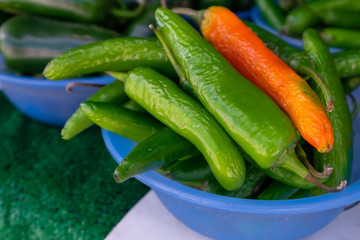 A closeup of a blue bowl of long hot green Chile peppers with the exception of one Mexican orange one. The fresh organic hot chili peppers still have their stems. The fresh produce is a raw plant.
