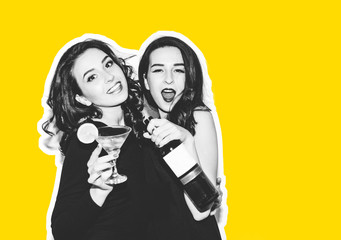 Two brunette sisters with long hair are drinking alcoholic cocktail and wine. Two beautiful girls in evening dress laughing and smiling. Bottle of wine. Yellow background.
