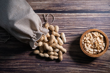 Peanuts in a bag and peeled peenuts in a bowl on wooden background. Healthy snack. Top view.