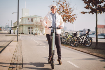 Tourist woman rent Electric scooter in danish capital Copenhagen. Female holding steering column knob with electric kick scooter handle on street in europe on sunny winter day