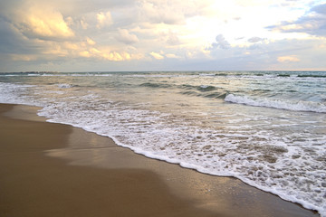A tropical beach with a colorful sunset, wet sand in the foreground of waves and overcast sky. Copy space