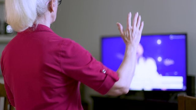 An older woman worshiping as she attends church virtually by streaming the online platform to her television because congregation and group fellowship is restricted during COVID19 pandemic.