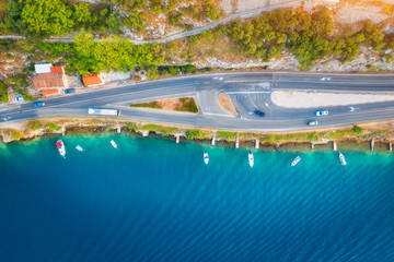 Fototapeta na wymiar Aerial view of road in beautiful green forest and boats in the sea at sunset in summer. Colorful landscape with asphalt roadway, blue water, trees. Top view from drone of highway in Croatia. Travel