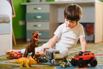 Cute little kid boy playing with lots of toy cars indoor. Happy preschooler having fun at home or nursery. Big collection of different vehicles. Happiness game.